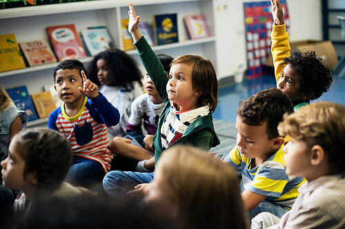 Young happy children sat on the floor at school with hands raised